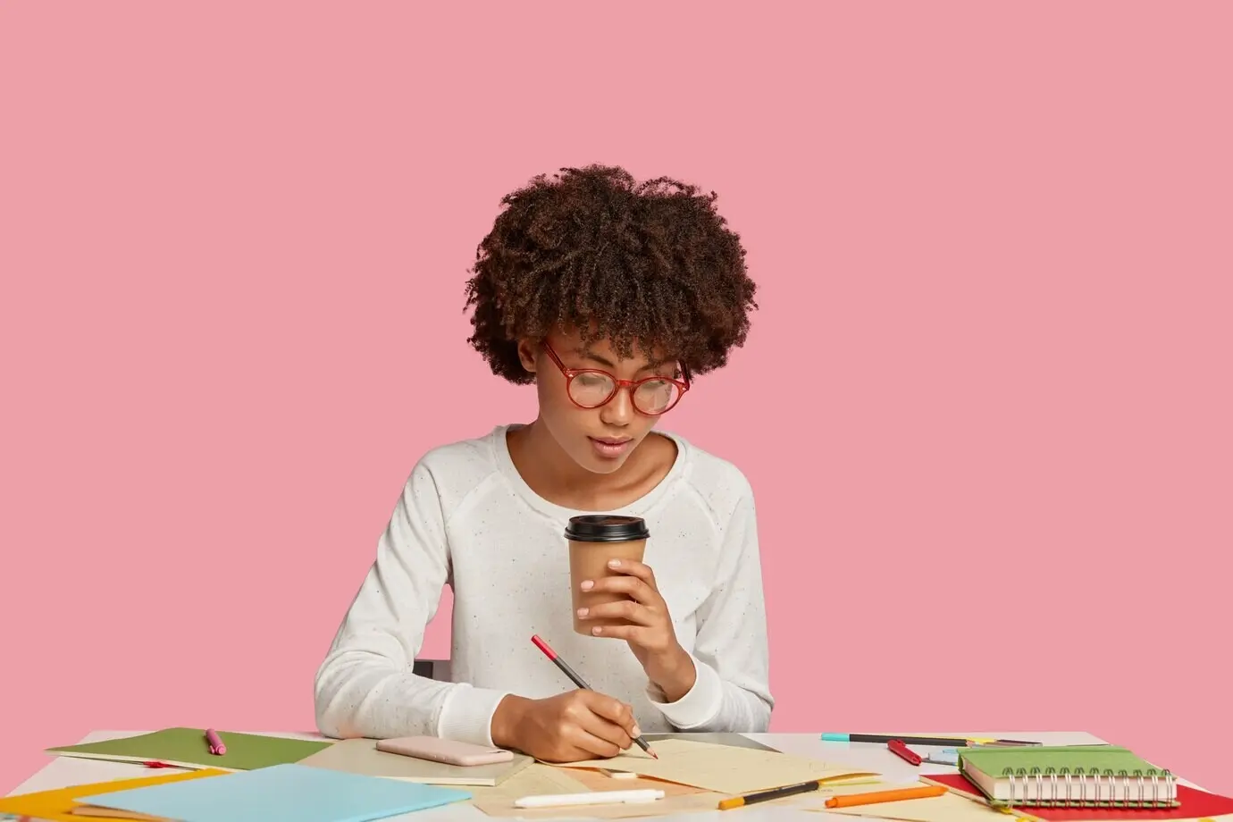 Красивая студентка позирует за столом на фоне розовой стены.